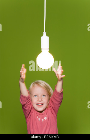 Little girl reaching for hanging light bulb Stock Photo