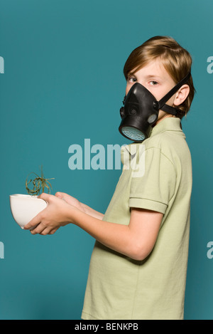 Boy wearing gas mask, holding wilted potted plant Stock Photo