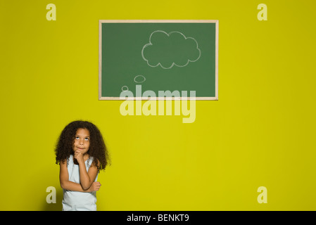 Little girl thinking, empty thought bubble on chalkboard overhead Stock Photo