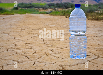 A water bottle on dry and cracked ground in the desert. Shallow depth of field Stock Photo