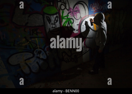 A teenage boy spraying graffiti on a wall in an alley Stock Photo