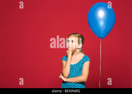 Girl with hand under chin, balloon suspended behind her Stock Photo