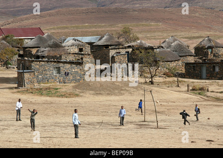 Children playing football in Basotho / Basuto village showing stone huts with thatched roofs in Lesotho, Africa Stock Photo