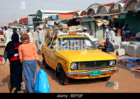 Street scene showing yellow taxi and Nubian people shopping at market in the city Omdurman, Khartoum, Sudan, North Africa Stock Photo