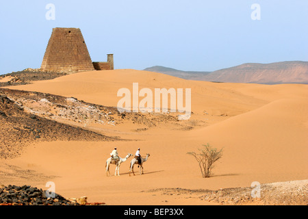 Pyramids of Meroe and two Nubian men dressed in thawbs riding dromedaries in the Nubian desert of Sudan, North Africa Stock Photo
