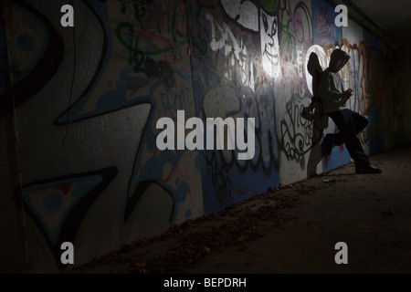 A teenage boy spraying graffiti on a wall in an alley Stock Photo