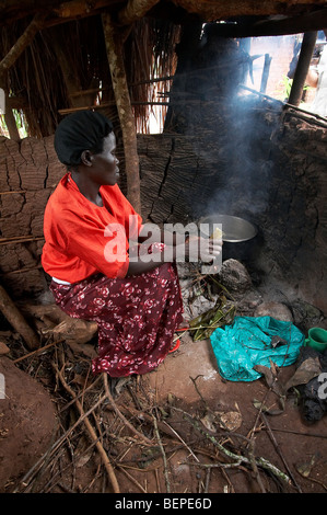 UGANDA Woman using traditional method of cooking on open fire in a smokey kitchen. Kayunga District. PHOTO by SEAN SPRAGUE Stock Photo