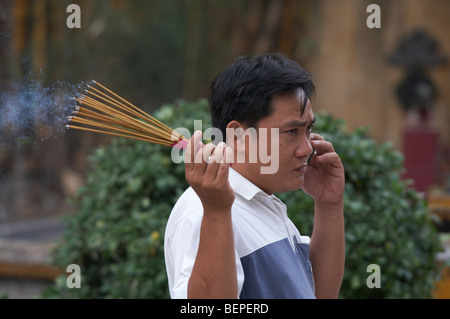 VIETNAM Saigon temple scene. Man with incense talking on cell phone. photograph by Sean Sprague 2008 Stock Photo