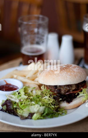 A burger and chips served in an English pub with an out of focus pint of beer visible behind. Stock Photo