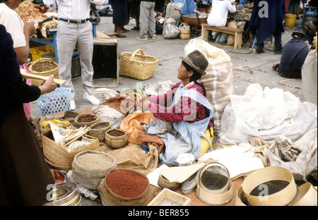 Woman sits on ground in midst of small sacks and baskets of spices. Ecuadorian Highland Marke Stock Photo