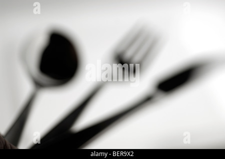 Spoon, fork and knife on white plate - out of focus Stock Photo