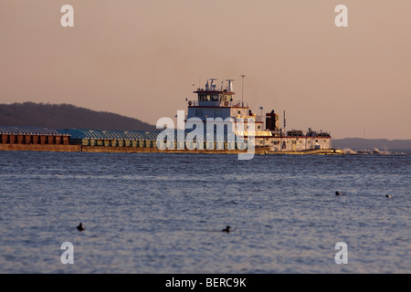 Pushing a few barges north along the Mississippi River, a large tug (tow) boat motors along the shores of Ft. Madison, IA. Stock Photo