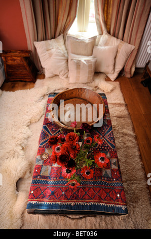 VASE OF FLOWERS ON A SMALL CHEST WITH SHEEPSKIN RUGS UK Stock Photo