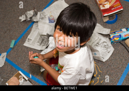 six year old boy working on making a vehicle out of recycled materials, smiles and looks up at camera Stock Photo