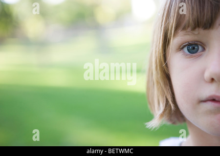 seven year old girl looking at camera with serious expression, green background, outdoors, closeup of face Stock Photo