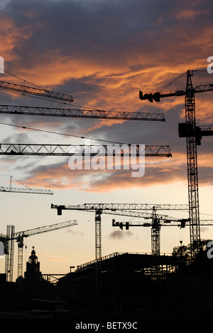 Tower construction cranes silhouetted against red sunset Stock Photo