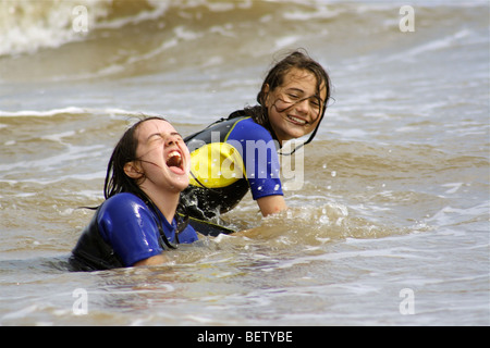 two girls swimming in the sea in wet suits having a great time playing in the waves