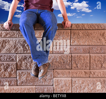 Man in blue jeans sitting outdoors on a brick wall. Stock Photo