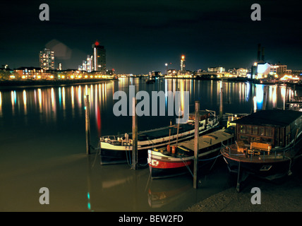 House boats moored off Chelsea embankment at night with Chelsea harbour and Battersea reach in the background Stock Photo