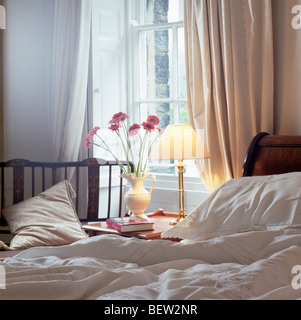 Lighted Lamp On Bedside Table In Front Of Window With Cream Curtains In Small Country Bedroom Stock Photo Alamy