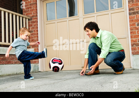 Father teaching son to play soccer on driveway Stock Photo