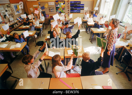 Elementary school children sitting at individual desks in Swedish classroom raising hands to answer questions from the teacher Stock Photo