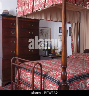 Four-poster bed with pink patterned drapes and bed cover in cottage bedroom with mahogany clothes-rail Stock Photo