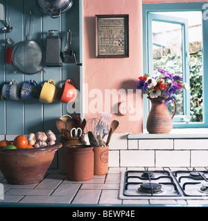 Utensils in earthen-ware jars on white-tiled worktop beside gas hob in pink kitchen with cups on blue panelled wall Stock Photo