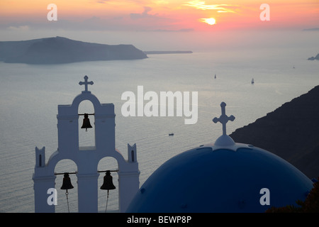 Greek white church with bell tower and blue dome, overlooking the sea at sunset, Santorini, Cyclades Islands, Greece. Stock Photo