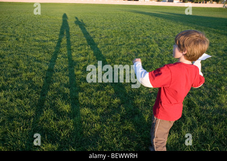 seven year old boy preparing to throw a paper airplane in an open field