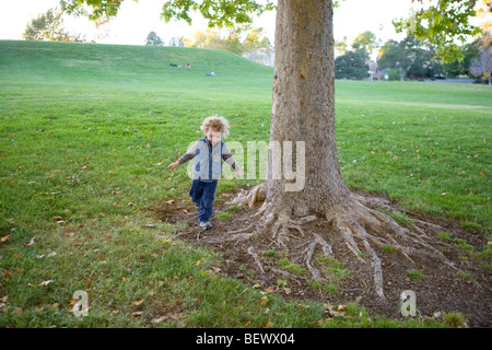 three year old boy running on the ground on tree roots, at a park, alone