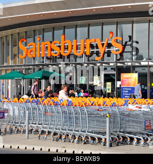 Sainsburys supermarket trolley park and entrance with Starbucks coffee shop Stock Photo