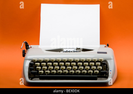 Old style typewriter with inserted blank paper over orange background Stock Photo