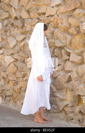 Woman on white scarf walking close to natural stone wall Stock Photo