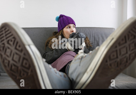 Saving heating coasts, young woman at home wearing a cap and gloves . Stock Photo