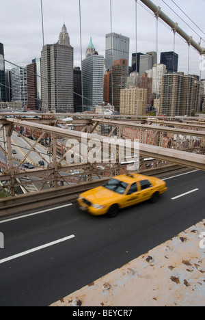 A yellow cab speeding over the Brooklyn Bridge, with the New York City skyline in the background. Stock Photo