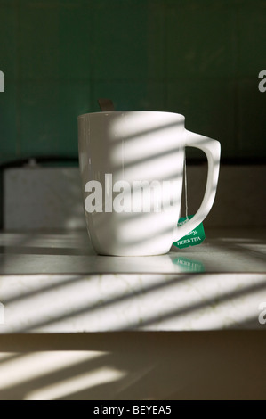 Sunlight streaming through venetian blinds casts striped shadows on a coffee and tea mug. Stock Photo
