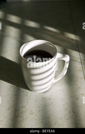 Sunlight streaming through venetian blinds casts striped shadows on a coffee mug. Stock Photo