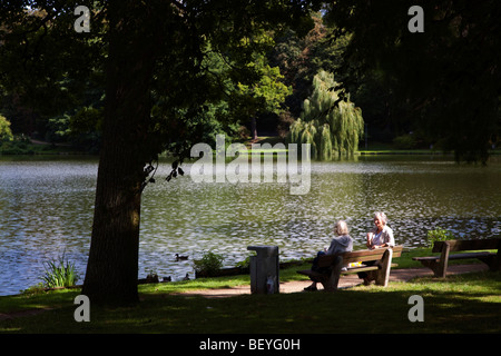 Two senior citizen women sitting in sunshine on park bench Lubeck Germany Stock Photo