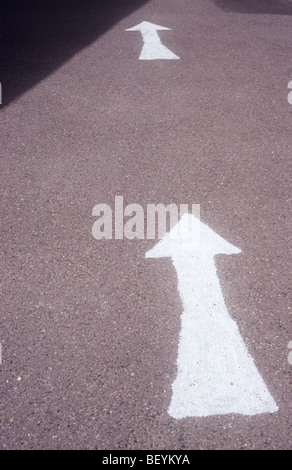 Two large white arrows in succession painted amateurishly on tarmac road surface partially in shade Stock Photo
