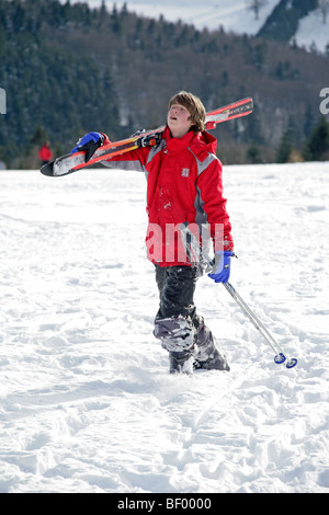 exhausted teenage boy carrying his skis uphill Stock Photo