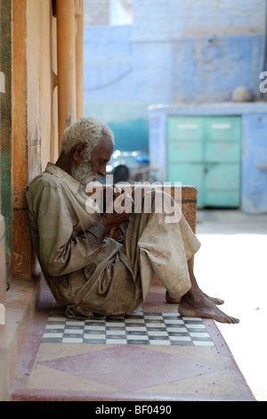 Old Indian man on doorstep lighting cigarette Stock Photo