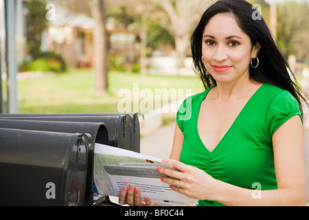 Woman holding mails and smiling near mailboxes Stock Photo