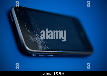 A damaged Apple iPhone device placed on a blue backround.  The main control screen has been cracked at the top. Stock Photo