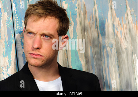 blue-eyed 30 year old man alone in front of peeling painted wooden door - looking away from the camera Stock Photo