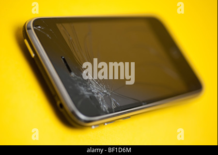 A damaged Apple iPhone device placed on a yellow backround.  The main control screen has been cracked at the top. Stock Photo