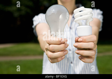 A young woman holding out a regular light bulb and an energy saving light bulb Stock Photo