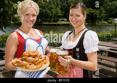 Two traditionally clothed German women serving pretzels and beer in a beer garden Stock Photo
