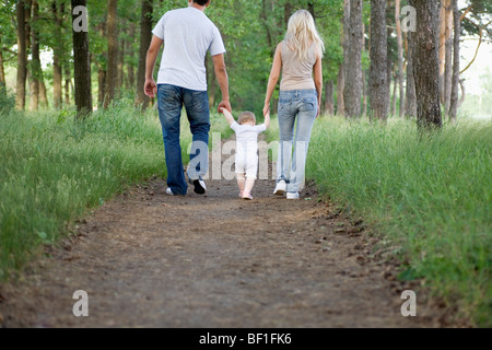 Two parents walking along a forest path with their young daughter Stock Photo