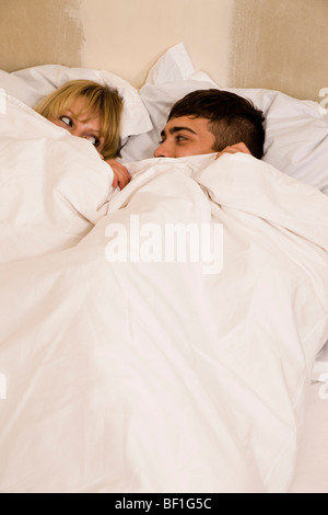 A young couple in bed with the duvet pulled up to their eyes Stock Photo